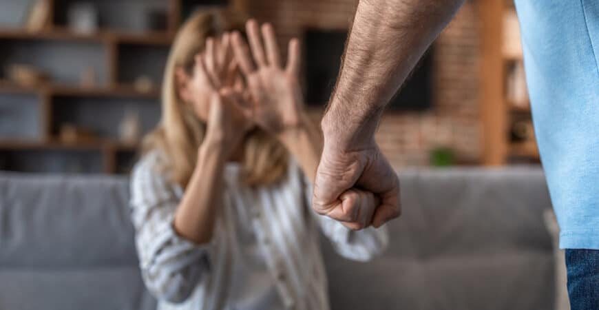 Sad crying adult caucasian wife covers her face, afraid of her aggressive husband in living room interior. Quarrel, beating, domestic violence and human emotions, relationship problems, scared at home